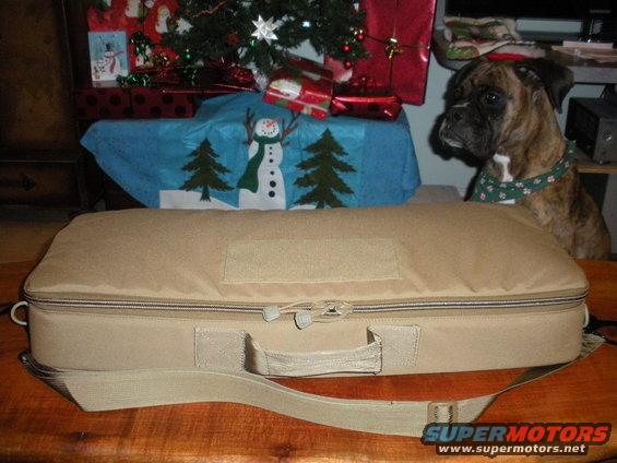 Tan rifle case on wooden table with boxer dog and Christmas decorations in background