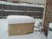 1972 Ford Ranchero - A generator sits covered in snow in a backyard setting, with a wooden fence and brick wall visible.