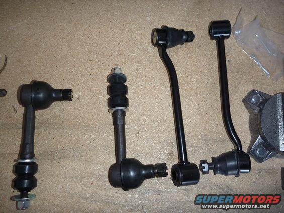 Several black suspension linkage parts laid out on a tan surface. Includes tie rod ends and sway bar links