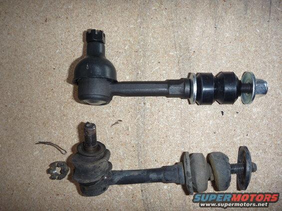 Two suspension stabilizer bar links, one new and one old, on a wooden surface. A nut and clip are to the left of the old link