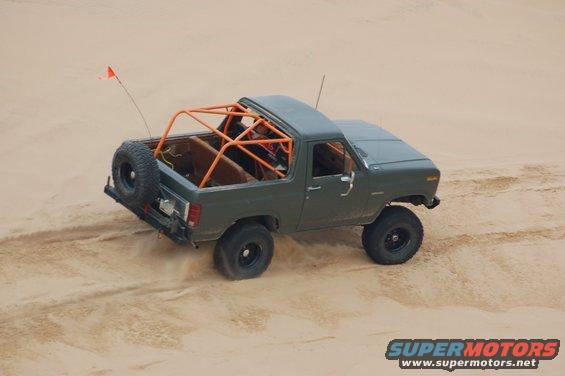 1982 Ford Bronco with roll cage and spare tire on rear, driving in sand dunes