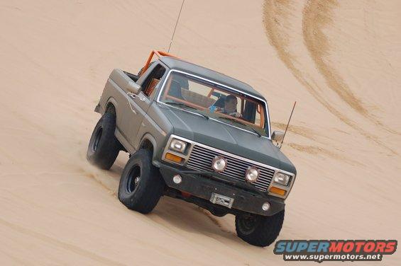 Ford Bronco driving on a sand dune with an orange roll cage visible inside