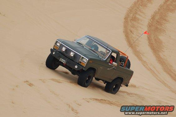 Green 1980s Ford Bronco climbing a sand dune with an orange roll cage