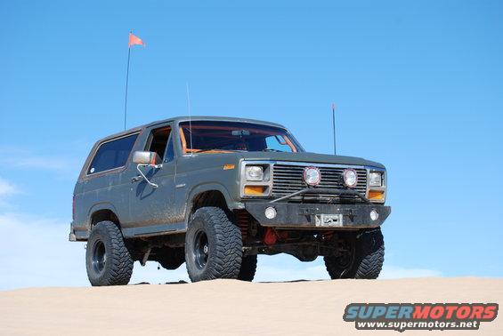 Gray Ford Bronco with off-road tires and bumper, parked on sand dunes