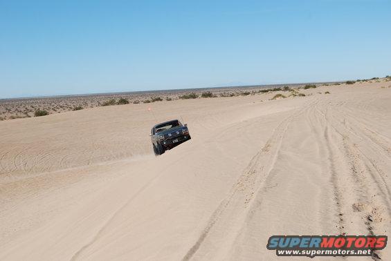 Dark blue 1980s SUV driving up a sand dune