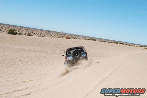 Dark SUV kicking up sand on a desert dune, spare tire mounted on rear door