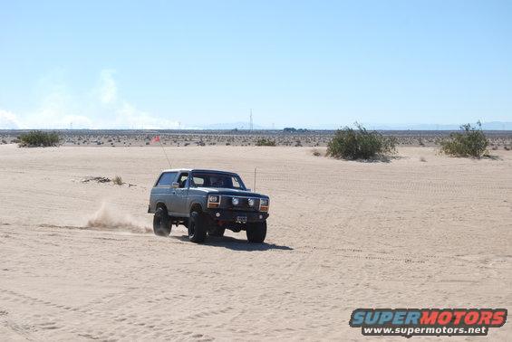 Gray SUV with off-road tires kicking up sand, front view