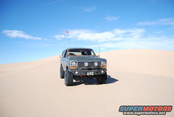 Gray 1980s Ford Bronco with off-road tires and bumper on sand dunes