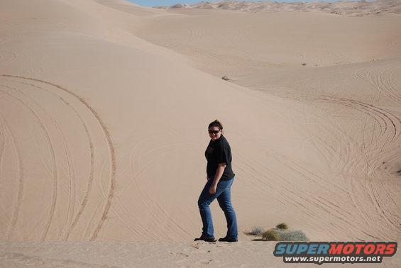 Person standing on a sand dune with tire tracks visible