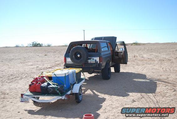 Dark SUV with spare tire on rear, towing a trailer loaded with coolers and gas cans