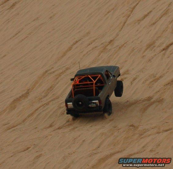 pickup truck with orange roll cage driving up a sand dune