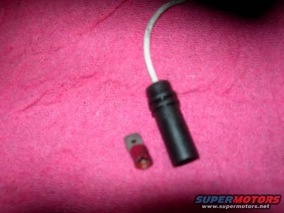 Black plastic connector with white wire and a small red and gray brake pad wear sensor on pink fabric