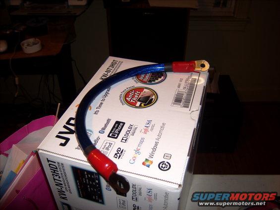 Blue battery cable with red ends and gold terminals sits on a JVC car stereo box