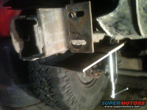 Close-up of a custom trailer hitch receiver being installed on a vehicle, showing metal brackets and a tire