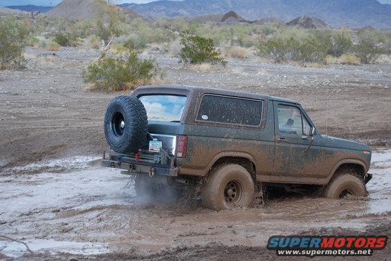 Green Ford Bronco stuck in mud, spare tire mounted on rear