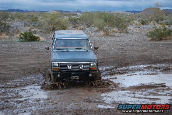 Gray Ford Bronco driving through mud, front view, with aftermarket lights