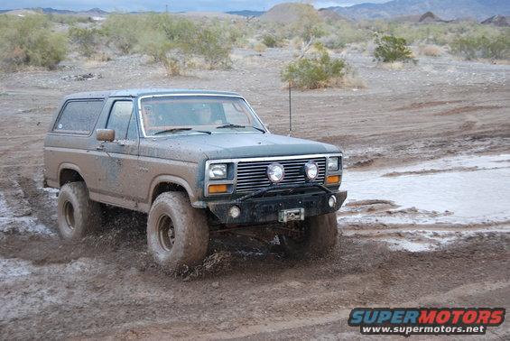 Muddy 1980 Ford Bronco driving through water and mud