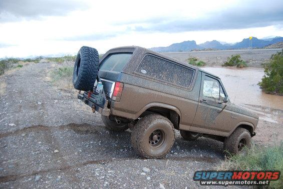 1982 Ford Bronco driving through muddy water, spare tire mounted on rear carrier