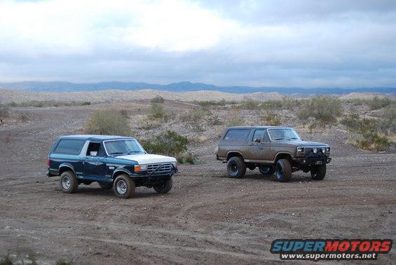 Two 1982 Ford Broncos parked in a desert with mountains in the background