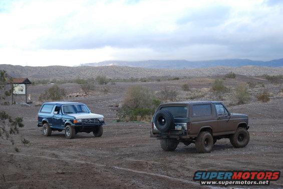 Brown Ford Bronco with spare tire on rear, blue Ford Bronco in background, desert scene
