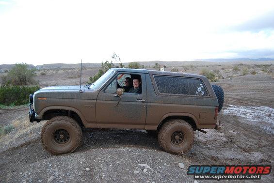 1982 Ford Bronco driving through mud with two people inside