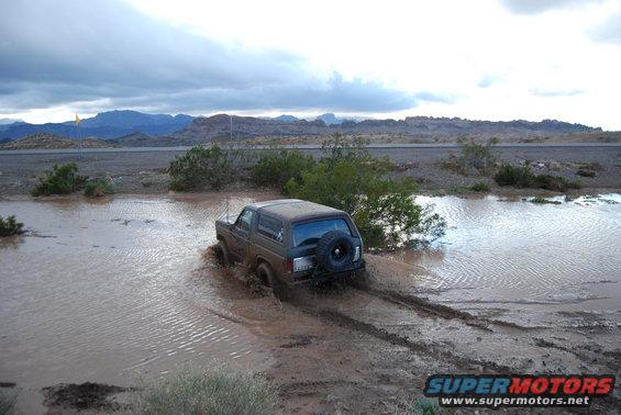 Ford Bronco driving through a muddy water puddle with mountains in the background