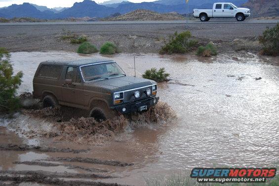 Brown 1982 Ford Bronco splashing through mud puddle
