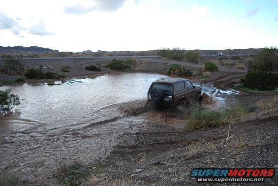 Brown Ford Bronco driving through muddy water, rear view