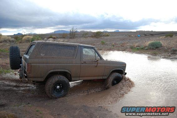 Brown Ford Bronco driving through a muddy puddle in a dry, barren landscape
