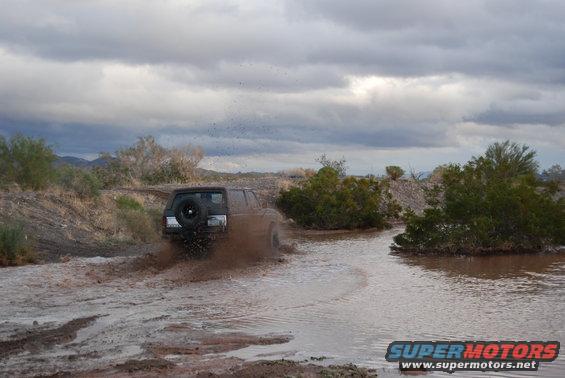 Off-road vehicle driving through muddy water with a spare tire on the back