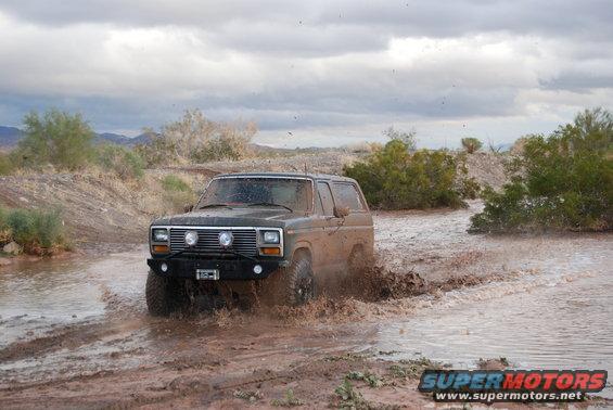Mud-splattered dark SUV driving through a muddy puddle, front grille visible