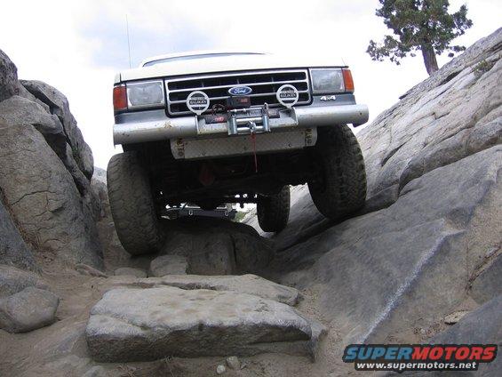 White Ford Bronco climbing over large rocks on a trail. It has a winch and 4x4 badging