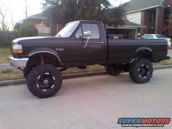 Dark pickup truck with lifted suspension and large tires, side view