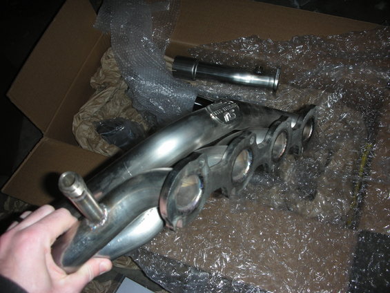 Hand holding stainless steel exhaust headers in a cardboard box with bubble wrap