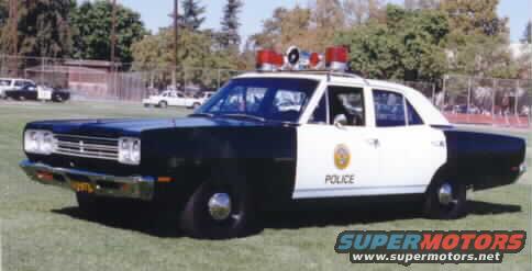 Black and white vintage Plymouth police sedan with roof beacons on grass
