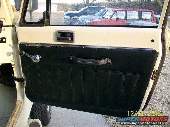 Interior door panel with chrome crank and black upholstery. Other vehicles visible outside