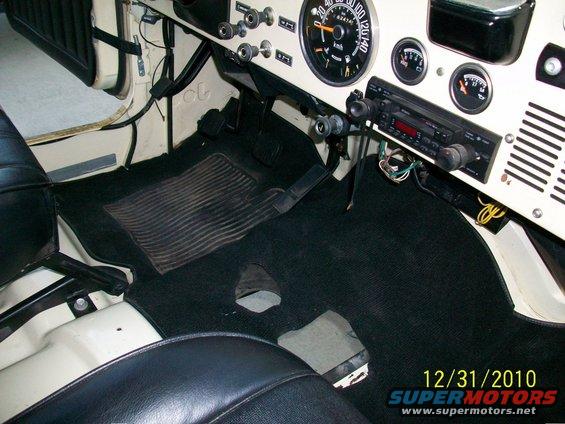 Jeep interior with black carpet and seats, showing dashboard gauges and radio