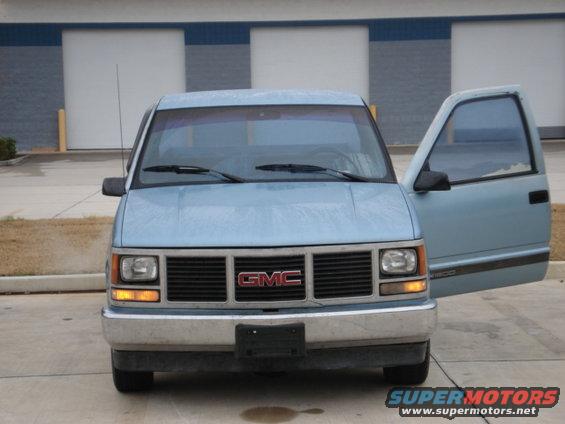 Front view of a light blue GMC pickup truck with the driver's door open. It has a black grille with a red GMC badge