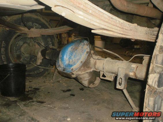 Close-up of a vehicle's rear axle, leaf springs, and tire. A blue differential cover is visible