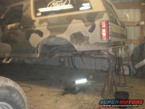 Camouflaged Ford Bronco on jack stands, rear axle removed, in a garage