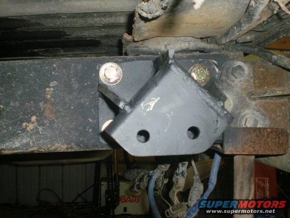 Custom bracket bolted to vehicle frame, likely for suspension modification. Wires hang below