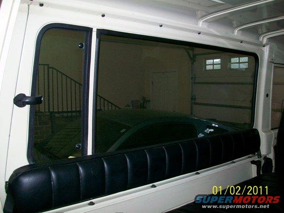 Interior view of a white vehicle looking out a window at a dark car in a garage