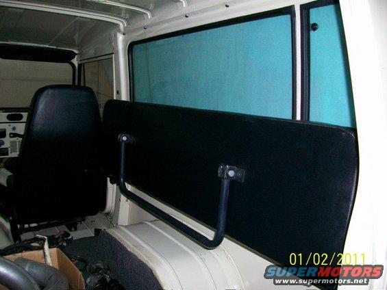 Interior view of a vehicle showing black seats and a black panel with metal supports. Blue tinted windows are visible