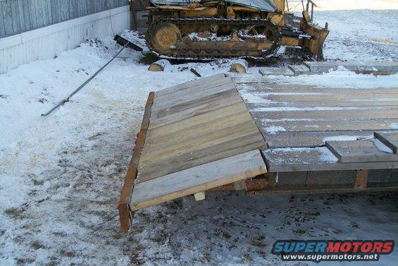 Trailer with wooden ramp and bulldozer in background
