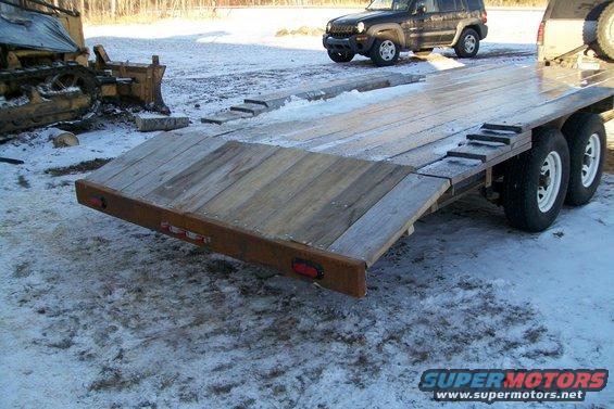 Flatbed trailer loaded with a bulldozer, parked near a black SUV in a snowy lot