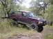 1996 Ford Bronco - A purple 1996 Ford Bronco navigates a wooded trail, with its front-right wheel high off the ground.
