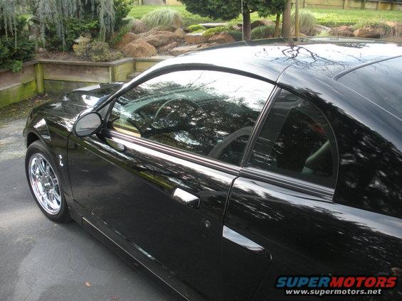 Black coupe with chrome wheels, side view. Interior visible through windows