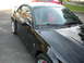 2003 Ford Mustang - Black 2003 Ford Mustang coupe with racing stripes and red interior, seen from a 3/4 front angle. Another red vehicle is partially visible i…