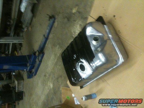 fuel tank with black coating on one side, sitting on cardboard next to a spray can