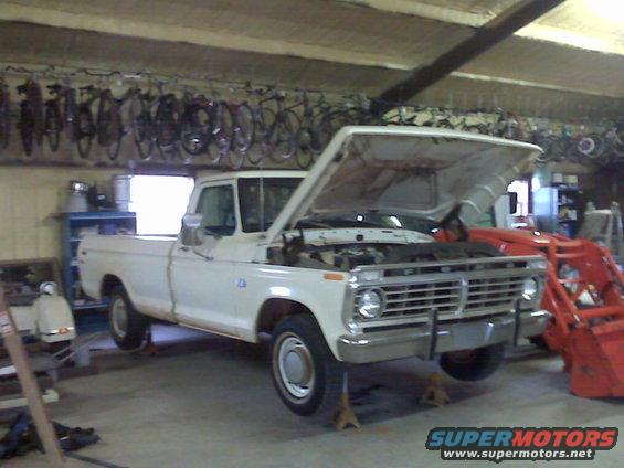 White 1973 Ford F-100 pickup truck with hood open, on jack stands, in a garage